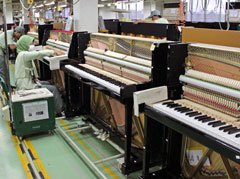 Workers assembling Yamaha upright pianos in a factory.