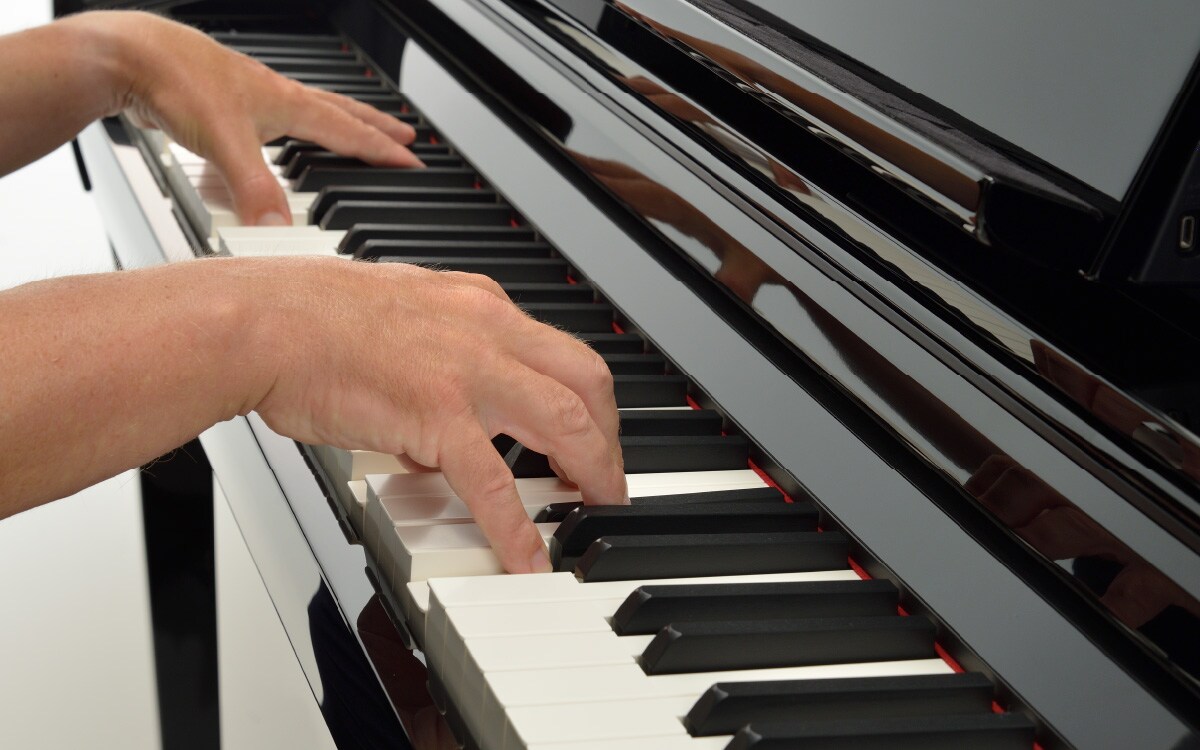 Hands playing the keys of a black Yamaha Clavinova piano