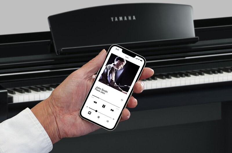 A smartphone playing audio in front of a Yamaha Clavinova piano.