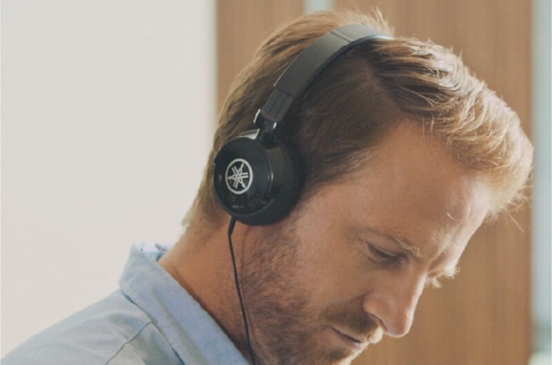 A person wearing headphones while listening to a Yamaha piano.
