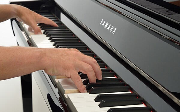 Close-up of hands playing the keys of a black Yamaha Clavinova piano.