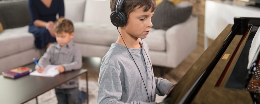 Young boy wearing headphones and playing a Yamaha Disklavier piano.