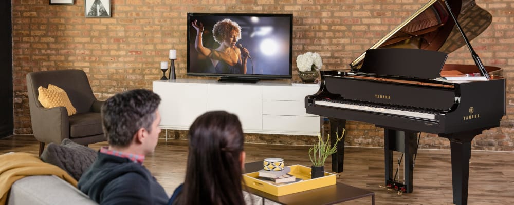 People watching a Yamaha Disklavier piano in a living room.