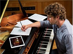 Man writing music at a Yamaha Disklavier grand piano with a tablet