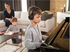 Boy wearing headphones playing a Yamaha Disklavier piano in a living room