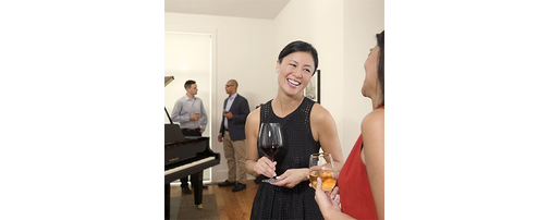 People socializing around a Yamaha grand piano at an indoor gathering.