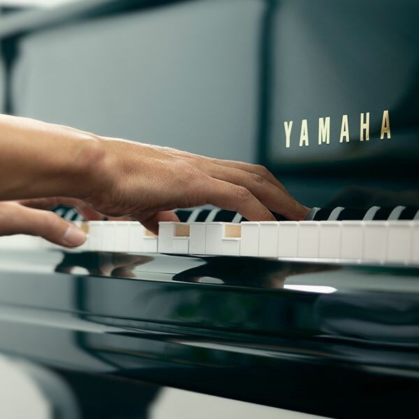 Hands playing the keys of a glossy black Yamaha grand piano.