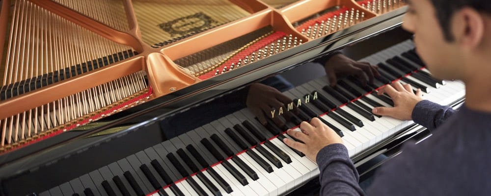 A young man playing a Yamaha baby grand piano with the lid open.