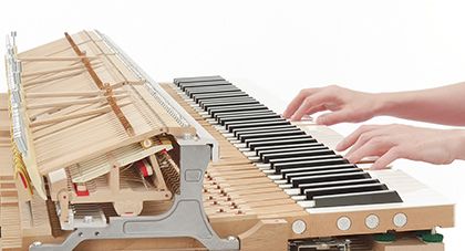 Hands playing exposed grand piano action mechanism of Yamaha N1X.