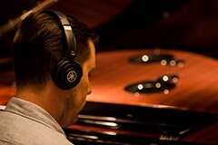 Person wearing Yamaha headphones while playing a grand piano.