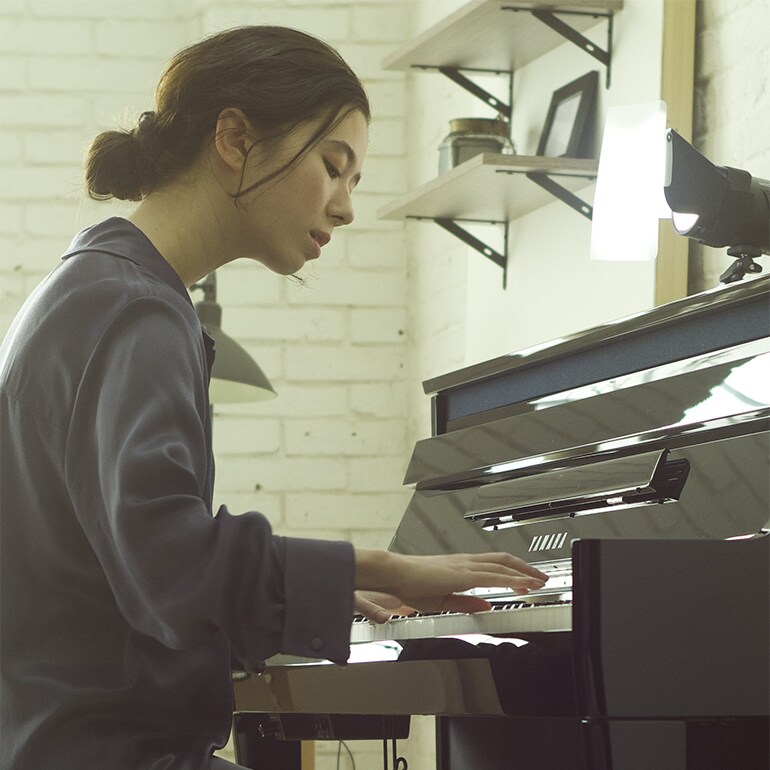 Young woman playing a Yamaha NU1XA AvantGrand piano indoors.
