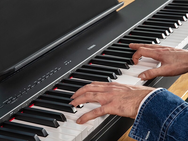 Hands playing the keys of a Yamaha P-225 digital piano.