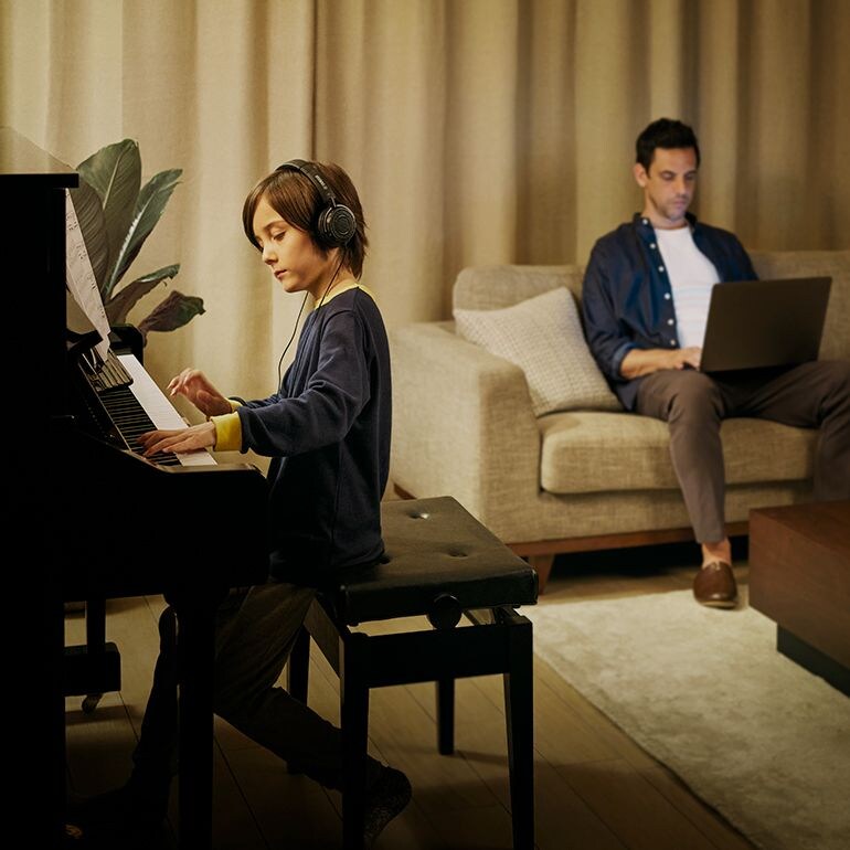 A child wearing headphones playing an upright SILENT Piano while an adult works nearby.