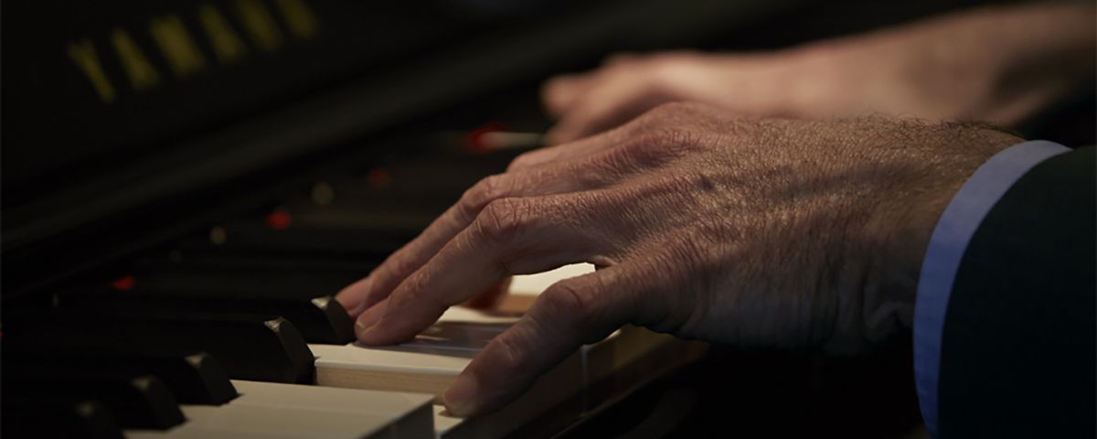 Close-up of hands playing a Yamaha upright piano.